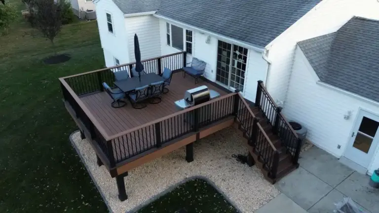 aerial-view-of-the-raised-residential-deck-with-black-post-cap-railing-and-outdoor-living-dining-set-area-with-grill-attached-on-the-white-house-with-multiple-windows-in-southeast-pa