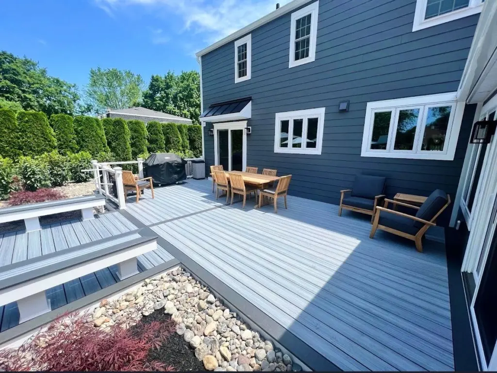 commercial-gray-deck-on-the-dark-blue-house-with-outdoor-living-dining-set-area-with-couch-and-covered-grill-featuring-grass-trees-and-sky-view-on-the-background-in-pottstown-pa