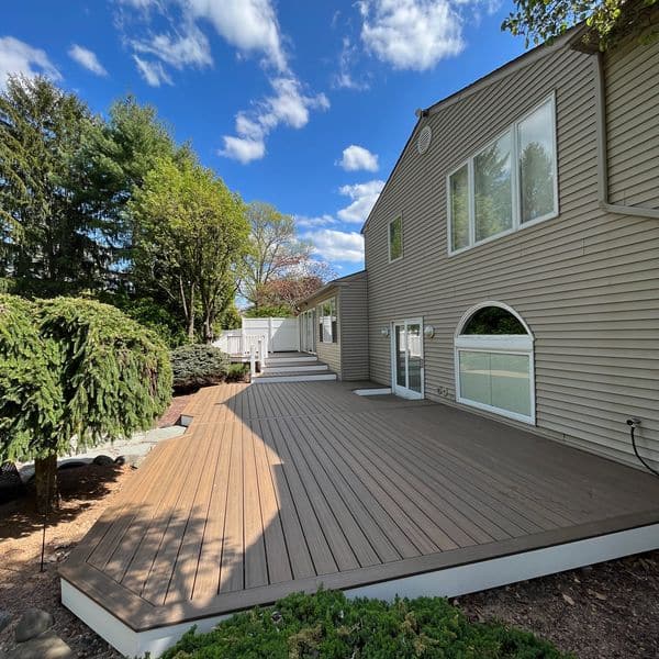 custom-residential-deck-framing-with-white-railing-and-white-wall-fence-on-the-beige-house-with-big-windows-featuring-trees-and-sky-view-on-the-background-in-southeast-pa